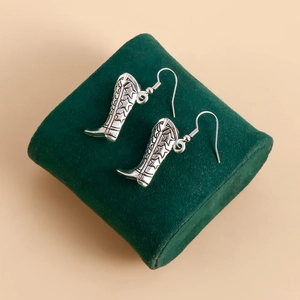 Détail de boucles d'oreilles bottes de cowboy argentées sur velours vert foncé