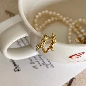 Close-up of minimalist gold twisted hoop earrings hanging on a white ceramic cup