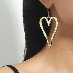 Detail of a large gold heart-shaped earring with lava texture worn by a model