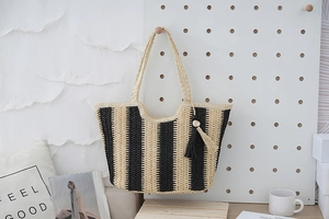 Detail shot of the vertical striped straw tote bag featuring a decorative fringe tassel