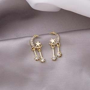 Macro detail of gold star and moon earrings with cubic zirconia on silk fabric