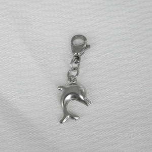 Close-up of a jumping silver dolphin pendant with lobster clasp on white fabric