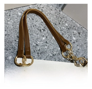 Close-up of brown leather shoulder strap with gold metal rings on a beige suede tote bag