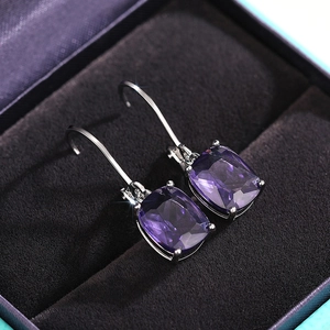 Macro shot of cushion-cut purple gemstone earrings with silver prong setting in a jewelry box