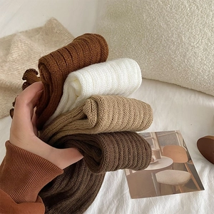 Close-up of ribbed knit texture on warm leg warmers in white, khaki, and brown tones