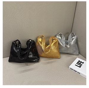 Trois sacs à bandoulière à paillettes en noir, or et argent posés sur un canapé
