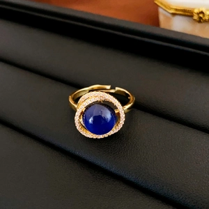 Close-up of golden adjustable ring with deep blue center stone and white zircon halo