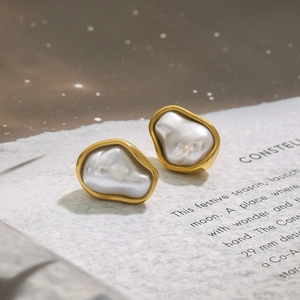 Close-up of elegant gold irregular earrings with white pearl inlay on textured paper