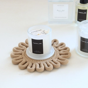 Detail of soy wax candle in glass jar on a hand-woven beige cotton heat-resistant mat