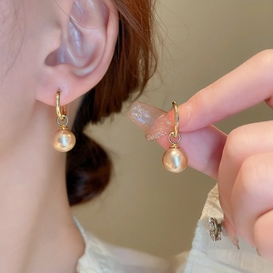 Détail de boucles d'oreilles anneaux dorés avec perles de champagne portées par un modèle