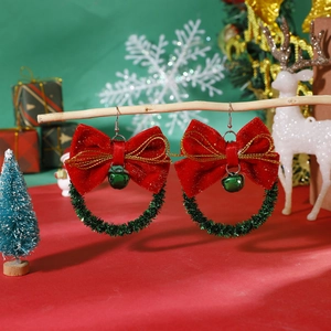 Close-up of Christmas wreath earrings with red bows and green bells on a wooden branch