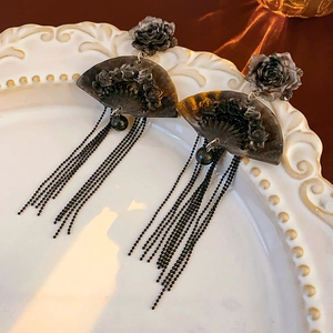 Macro detail of Chinese fan-shaped earrings with flower accents and black bead tassels