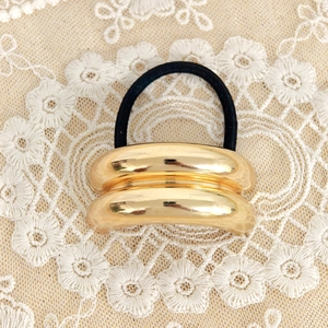 Close-up of golden double-layer curved metal hair tie on a white floral lace fabric