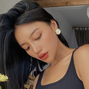 Close-up of model wearing gold-plated round earrings with white enamel inlay for women