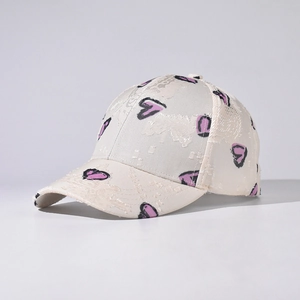 Detail of cream baseball cap with lace texture and pink heart graphics from a side view