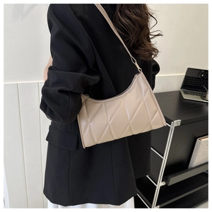 Model wearing a beige quilted baguette bag on shoulder in a modern office setting