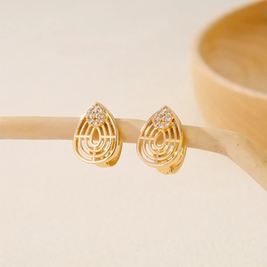 Macro shot of gold-plated teardrop earrings with zircon inlay on a natural wood branch
