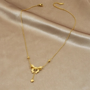 Collier élégant doré avec nœud et pendentif cœur sur fond de satin champagne