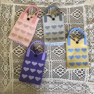 Detail of four colorful knitted mini bags with heart patterns on white lace fabric