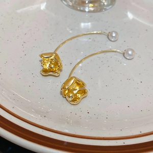 Detailed macro view of elegant gold pearl drop earrings on a minimalist ceramic plate