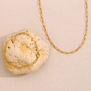 Detailed view of gold paperclip chain necklace and bracelet set on stone decor