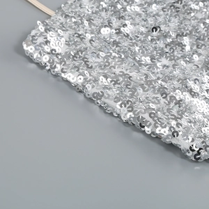 Detailed close-up of shiny silver sequins on white mesh fabric for evening dress