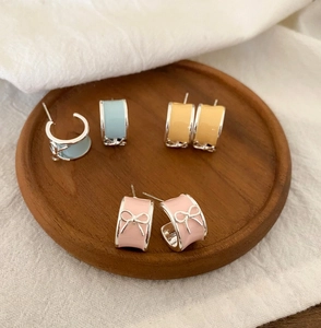 Detail of elegant bow knot enamel hoop earrings in pink, yellow and blue shades.