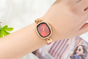 Detail of a red oval watch dial with gold rhinestone bezel on a model wrist