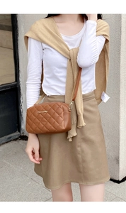 Detailed view of a brown quilted camera bag with gold logo on a model in sunlight