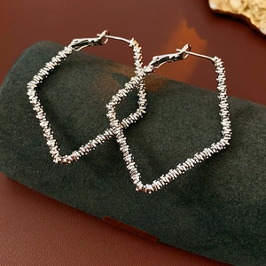 Detailed close-up of textured silver rhombus earrings on a dark stone display base