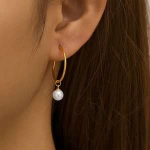Close-up of elegant gold hoop earrings with white pearl pendants worn by a female model