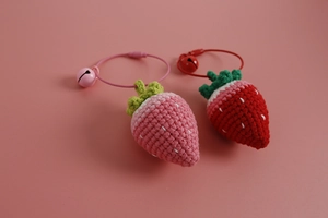 Detail of handmade crochet strawberry charms in pink and red with bells and rings