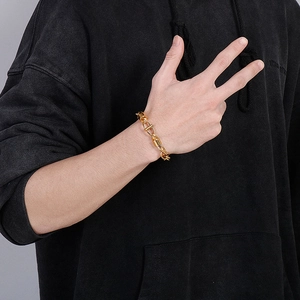 Détail d'un bracelet gourmette doré pour homme porté sur un fond noir avec maille torsadée