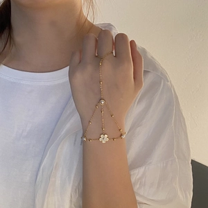 Detailed view of a gold-tone finger bracelet with a white five-petal flower and pearl beads