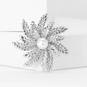 Macro detail of silver wheat snowflake brooch with pearl inlay on a white background
