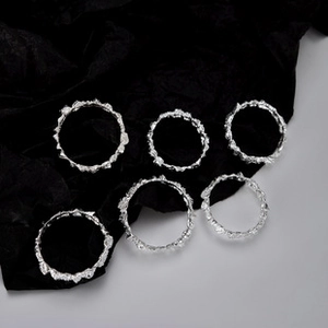 Detail of six S925 sterling silver rings with irregular melted texture on black fabric