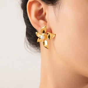 Elegant gold flower stud earrings with pearl center detail shown on model's ear