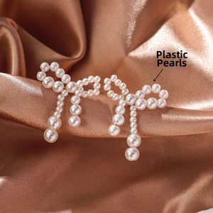 Close-up of elegant bow-shaped pearl earrings with tassels on silk fabric
