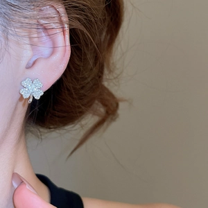 Close-up of sparkling silver clover stud earrings worn by a model in a warm setting
