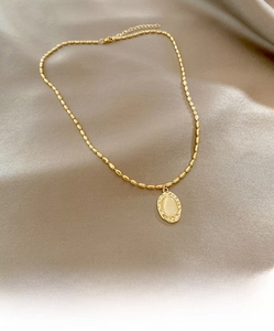 Close-up of golden beaded necklace featuring an oval cat eye stone pendant on champagne satin