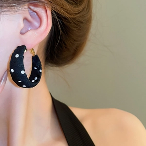 Close-up of black polka dot fabric wrapped hoop earrings on model with soft lighting