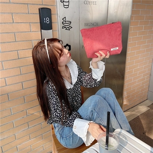 Pink corduroy makeup pouch held by hand in a chic city cafe street style setting