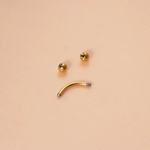 Golden titanium horseshoe barbell for septum or lip piercing on a beige background