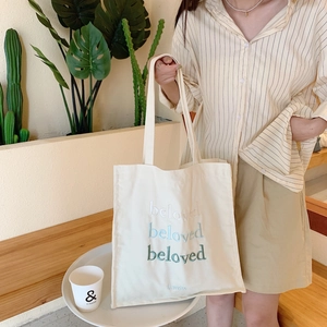 Detail of off-white canvas tote bag featuring green beloved gradient embroidery text