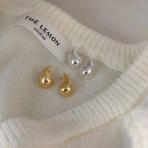 Detail of polished gold and silver teardrop earrings on a white ribbed knit background