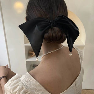 Elegant large black satin bow hair clip with pearl charms on a stylish hair bun