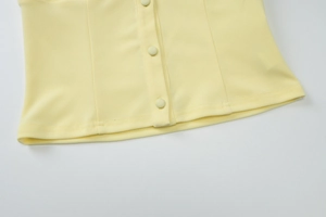 Detail view of the pale yellow vest showing neat fabric texture and matching cloth buttons