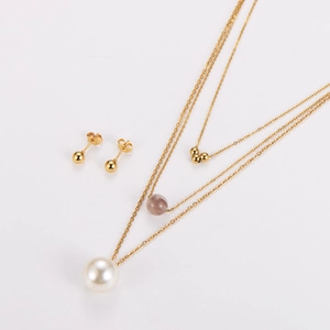 Détail du collier doré à trois couches avec perle brune, pendentif perle blanche et boucles