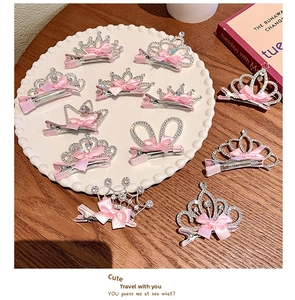 Detail of 11-piece crown hair clips set with pink bows and rhinestones on a tray