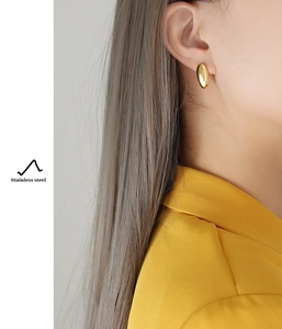 Close-up of a minimalist golden rice-shaped stud earring made of polished stainless steel